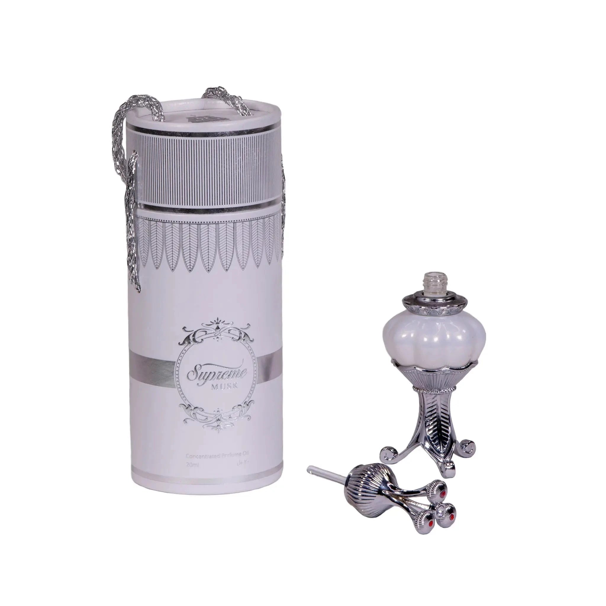 The image displays two items related to fragrance products on a white background. To the left is a cylindrical container adorned with a decorative silver chain, labeled "Supreme MUSK" with additional text below stating "Concentrated Perfume Oil 20ml." The container has a white label with an intricate, decorative border and a classic ornate emblem in the center. The bottle's top has a textured design with a tapered middle and flared ends, characteristic of vintage perfume dabber.