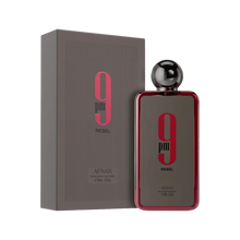 A rectangular fragrance bottle from Afnan labeled “9 pm Rebel,” featuring a metallic spherical cap and a glossy red border around a dark gray front, positioned beside a matching gray box emblazoned with pink and black branding.