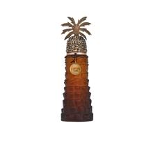 The image shows a unique perfume bottle by Lattafa Pride. The bottle has a distinctive textured design resembling the bark of a palm tree in a brown gradient color. Topping the bottle is an ornate silver cap designed to mimic a palm tree, complete with de
