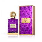 The image features a luxurious purple glass perfume bottle with a golden, textured cap next to its packaging. The bottle has a label with "Amethyst Khozam" written in both Arabic and English, signifying the fragrance's name from the brand Ibraheem Al Qurashi. The design of the bottle has a faceted pattern, giving it a jewel-like appearance. The packaging box is gold with a purple faceted design, complementing the bottle's design, and has a label that matches the one on the bottle.