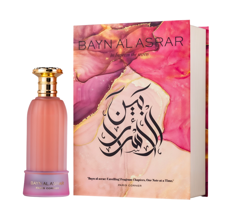 A soft, peachy-pink frosted glass bottle of Bayn Al Asrar by Paris Corner, topped with a gold cap, displayed next to a book-style box adorned with marbled swirls of pink and gold and bold Arabic calligraphy on the cover.