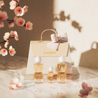 Laverne Sense Forever perfume trio arranged before a textured gift bag, with soft pink blossoms and warm light.