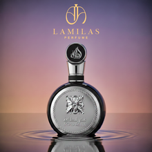 Fakhar Lattafa men's perfume, a dark round bottle with a silver ornate label and cap, standing in water against a gradient background.