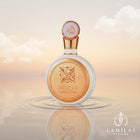 The white and gold Fakhar Lattafa Women perfume bottle is reflected in rippling water beneath a warm, cloudy sky.
