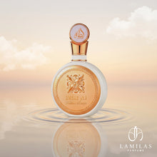 The white and gold Fakhar Lattafa Women perfume bottle is reflected in rippling water beneath a warm, cloudy sky.