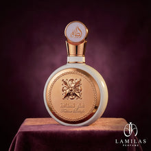 Elegant Fakhar Lattafa perfume bottle, white and gold, featuring an ornate metal plate, displayed on draped purple velvet.