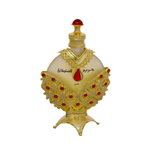 The image displays an opulent perfume bottle with a white background. The body of the bottle is a pale, translucent yellow, topped with a bright red cap resembling a gemstone.