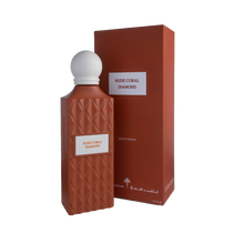 A sophisticated bottle of Nude Coral Diamond Eau e Parfum by Ibraheem Al-Qurashi, displayed next to its matching box. The bottle features a matte, coral-colored geometric texture with a diamond pattern and a white rectangular label that reads 'NUDE CORAL DIAMOND' in red text. It is topped with a smooth, rounded white cap. The packaging mirrors the coral color and minimalist aesthetic, with the same label and white brand markings near the base.
