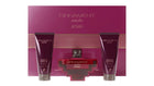 The image shows a beauty product set by AFNAN called "ORNAMENT purple allure". It includes two deep purple colored tubes labeled as "ENERGIZING SHOWER GEL POUR FEMME" and a matching perfume bottle in the center. The bottle has a square base with a red body and a cross-shaped metallic silver design embracing it. The cap appears to be a silver metallic color as well. Behind the products is a large cardboard packaging with the same deep purple color and a textured pattern.