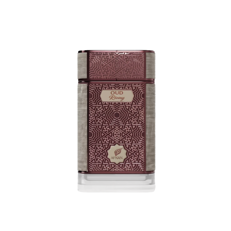 The image shows a rectangular perfume bottle with a sophisticated design. The bottle is predominantly a rich, dark maroon color with intricate, embossed geometric patterns that give it a textured look. There is a silver-colored, textured band that wraps horizontally around the bottle, dividing it roughly into thirds. Above this band is the brand name "AFNAN" in a stylized emblem, and below it is the fragrance name "OUD Rising" in a simple, elegant font on a cream-colored label.