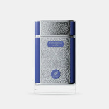 The image presents a perfume bottle with an elegant design. The bottle is clear glass with an intricate white geometric pattern covering most of its surface. It has a solid navy blue cap and a matching navy blue band that runs horizontally around the center of the bottle, providing a bold contrast to the white pattern. 