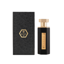 A sleek and elegant bottle of Reef 33 perfume by Reef Perfumes, positioned beside its matching box. The bottle is tall and angular, finished in glossy black with a vertical gold label engraved with 'REEF 33' and a crown emblem. It is topped with a polished gold hexagonal cap. The accompanying black box features an embossed rose pattern and a gold hexagon with the brand and fragrance name, reflecting a luxurious and refined aesthetic.