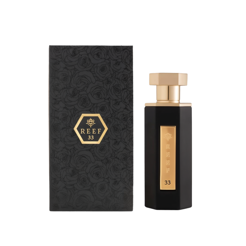 A sleek and elegant bottle of Reef 33 perfume by Reef Perfumes, positioned beside its matching box. The bottle is tall and angular, finished in glossy black with a vertical gold label engraved with 'REEF 33' and a crown emblem. It is topped with a polished gold hexagonal cap. The accompanying black box features an embossed rose pattern and a gold hexagon with the brand and fragrance name, reflecting a luxurious and refined aesthetic.