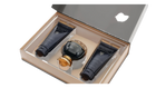 The image shows an elegant gift set by Afnan Perfumes from their "SOUVENIR Desert Rose" collection. The set is displayed in a beige presentation box with a clear lid, revealing its contents. Inside, there is a dark, glossy perfume bottle with a spherical design and a golden cap, positioned centrally. On either side of the perfume bottle are two matching dark tubes.  Both tubes and the perfume bottle feature the "SOUVENIR Desert Rose" branding in elegant gold lettering