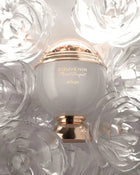 The image shows a perfume bottle with a clean and elegant design. The bottle has a spherical white body with a golden band that reads "SOUVENIR Floral Bouquet AFNAN." Above the band is a clear dome, encasing what appears to be a cluster of golden petals or flakes, giving a sense of luxury. The bottle rests on a golden pedestal base that complements the golden accents.