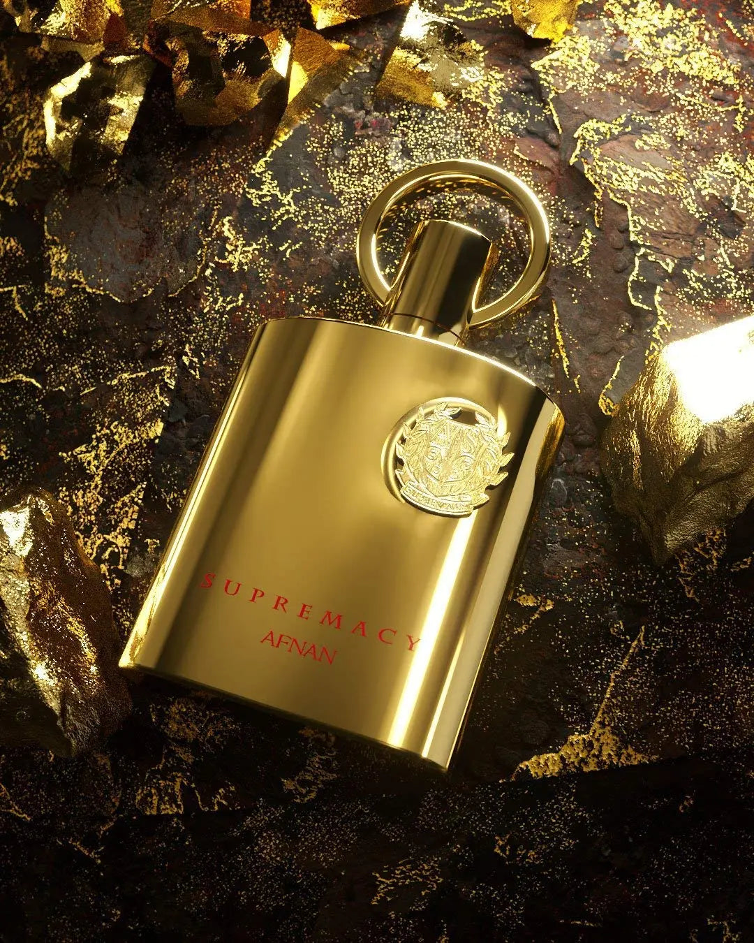The image depicts a glossy gold perfume bottle with a smooth, reflective finish, placed against a dramatic background adorned with gold leaf fragments on a dark surface that resembles a combination of black rock and molten gold. The bottle has a circular cap with a loop on top, suggesting an element of practicality or design flair.   "SUPREMACY AFNAN" printed beneath it in a sophisticated red font. The luxurious setting and the bottle's design convey an air of elegance and exclusivity.